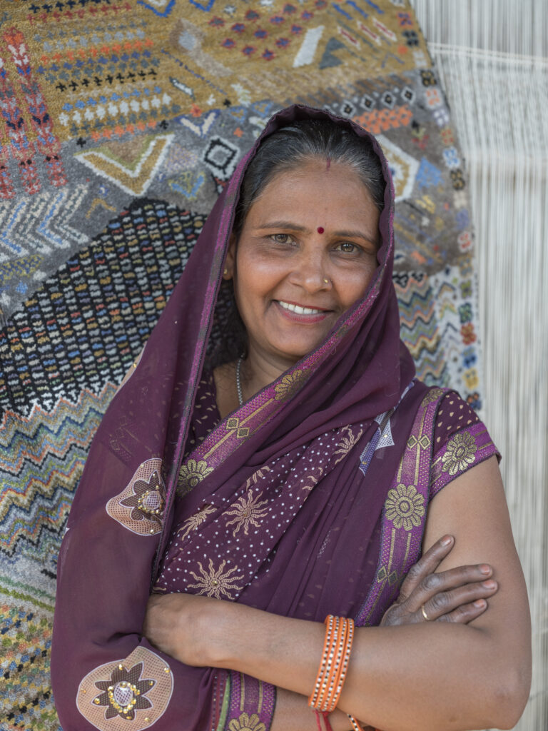 An artisan stands in front of her handmade one-of-a-kind rug