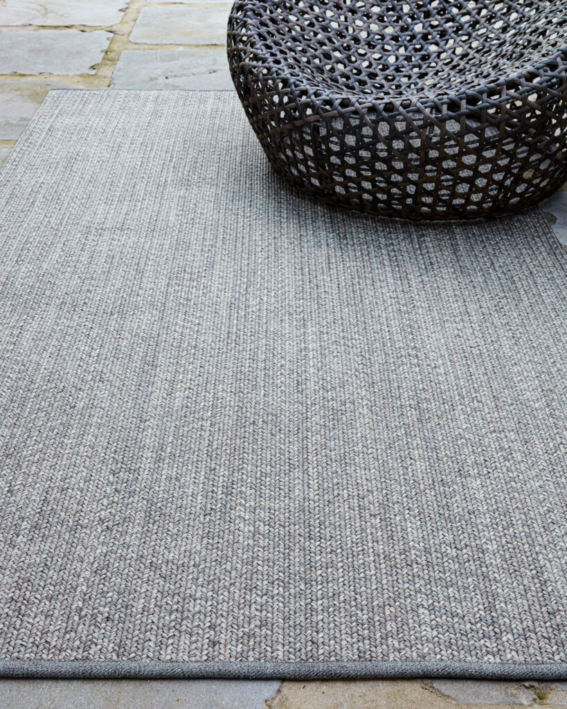 A neutral colored indoor/outdoor rug under a woven chair