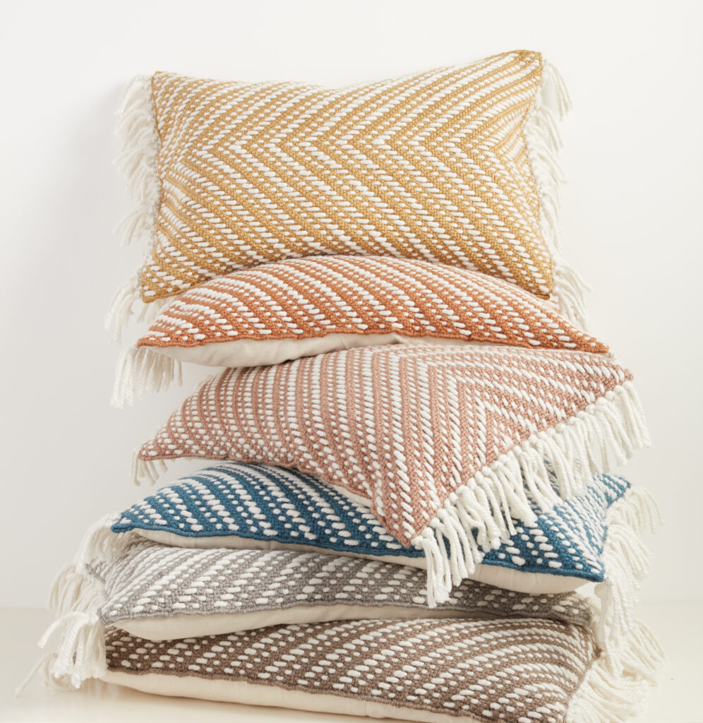 A stack of six woven indoor/outdoor pillows with tassels