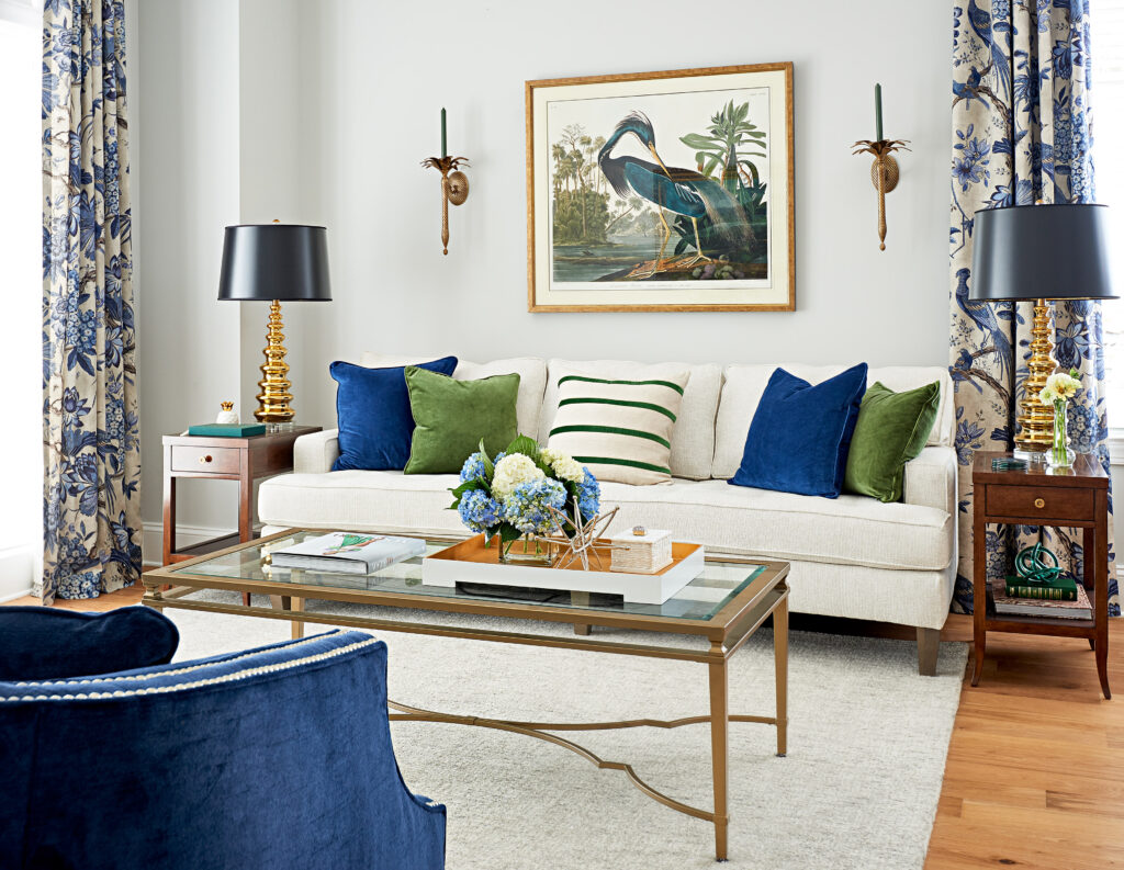 A living room with white couch, blue and green pillows, and floral patterns drapes