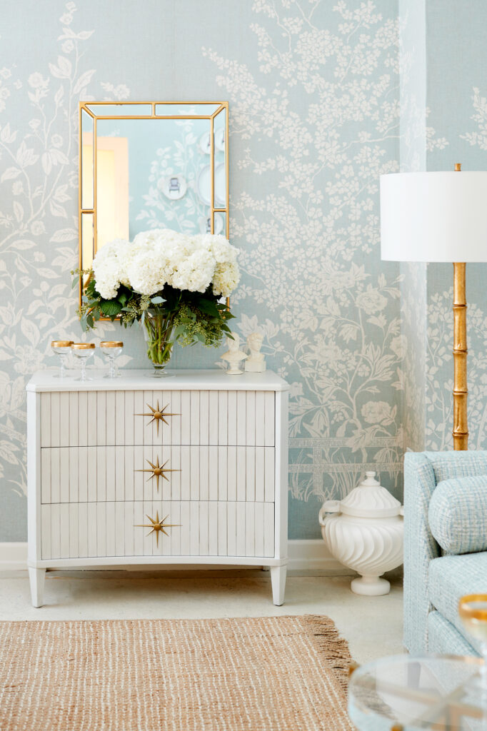 A living room with cream chest, mirror, standing lamp and light blue and white wallcovering