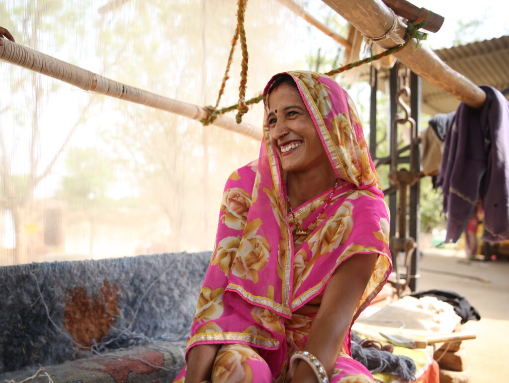 a woman artisan in a pink and gold sari sits at a loom