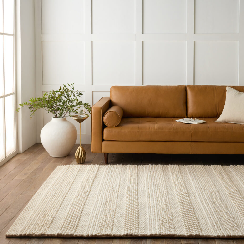 A sitting room with a leather sofa, white paneled walls, and a textured rug in a cream hue