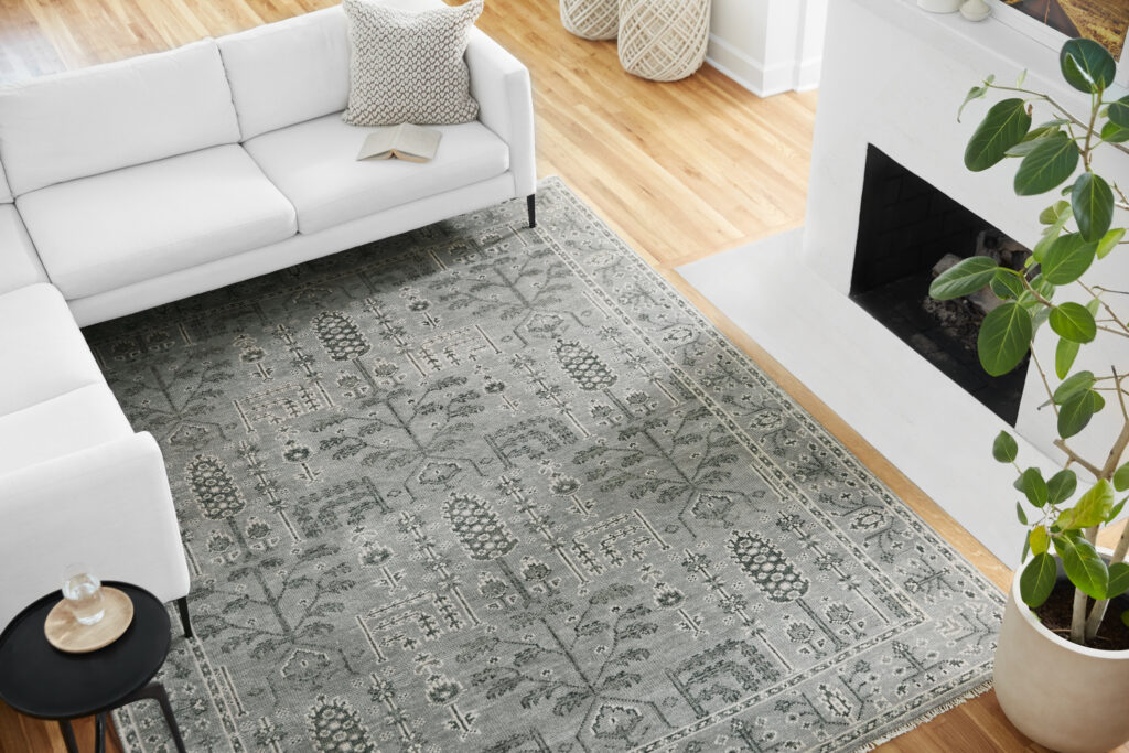 A blue and gray patterned rug in a living room with white section couch and white fireplace.
