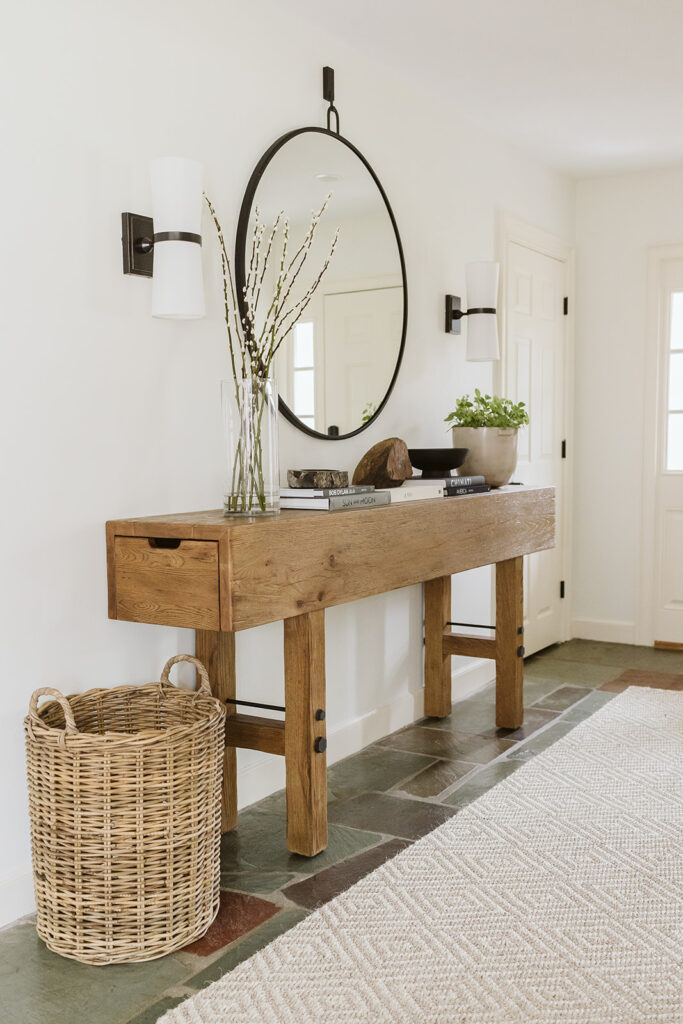 A natural rug in an entryway with a wooden console and round mirror