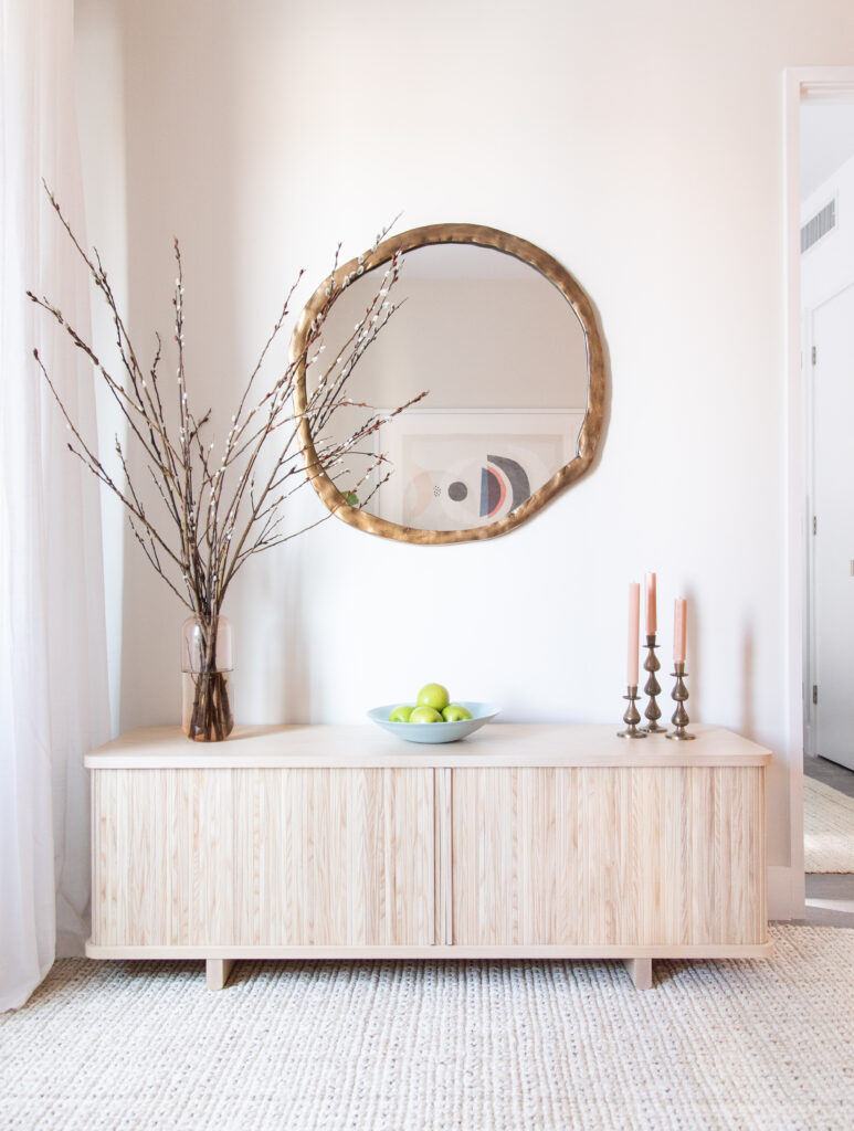 A credenza with a circular mirror, accent pieces, and natural rug underneath