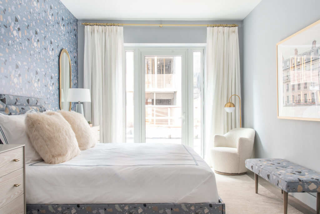A bedroom with blue patterned wallpaper, white bed and light gray rug