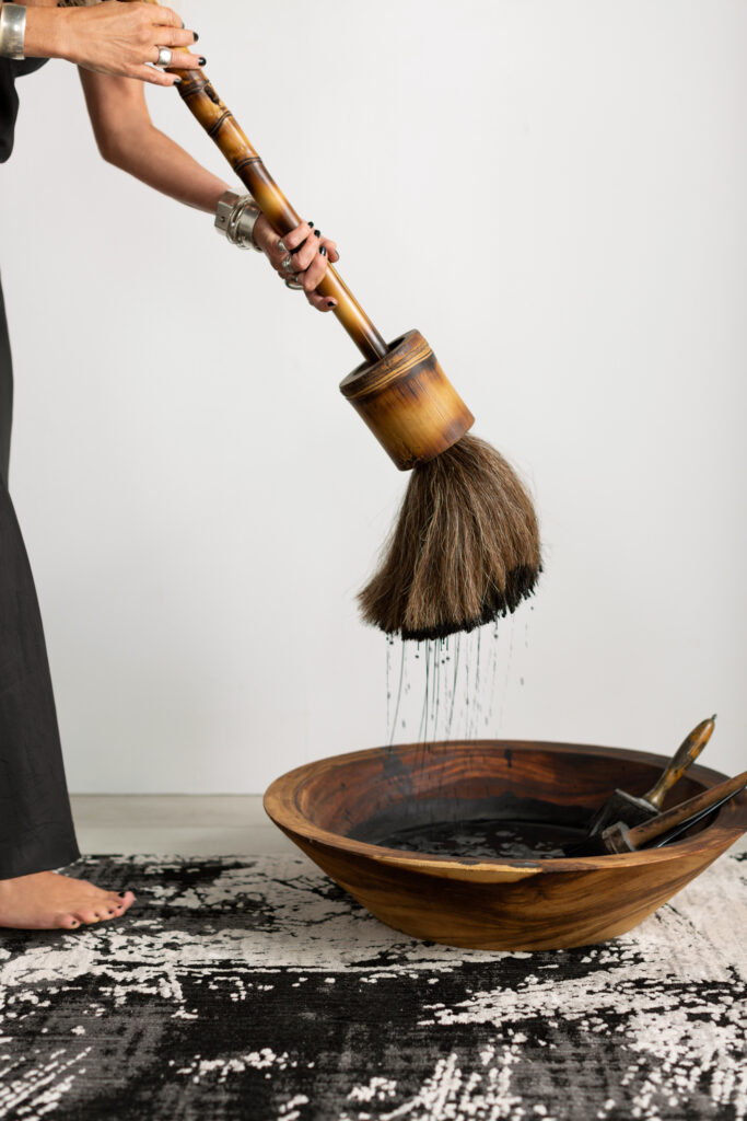 An artist with a large broom starts her Japanese ink art mural