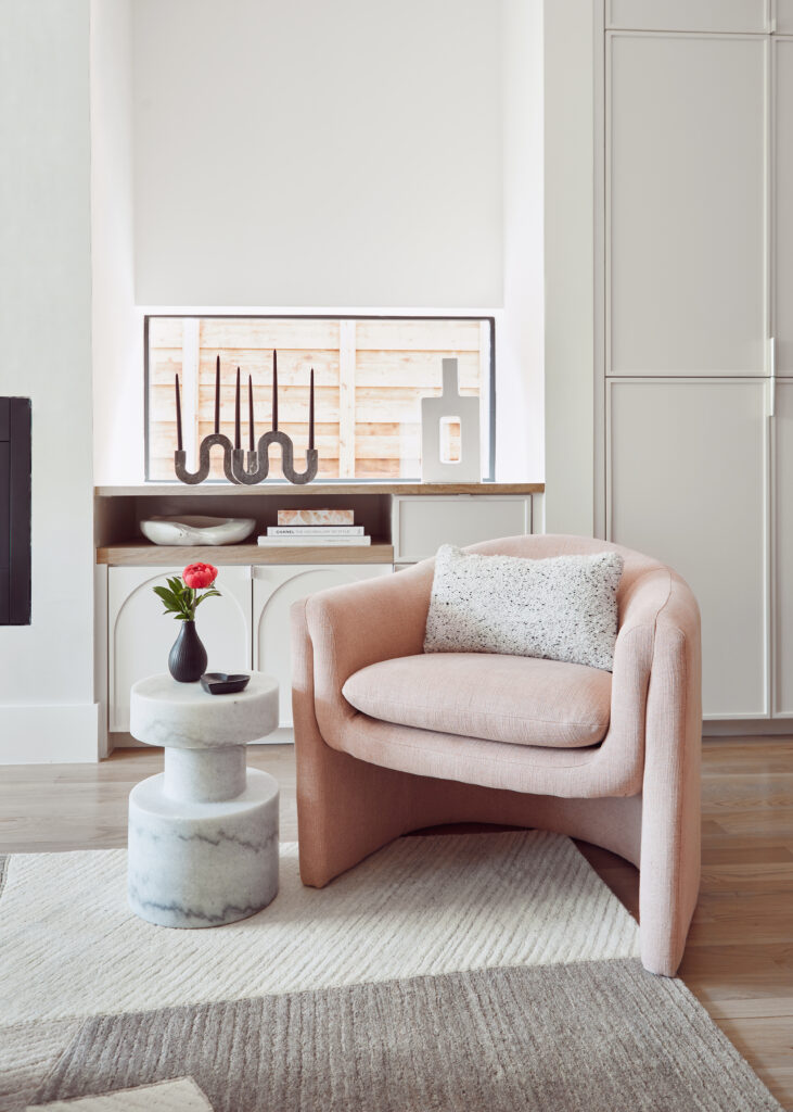 A pink modern chair with stone pedestal side table sit atop a gray and cream rug