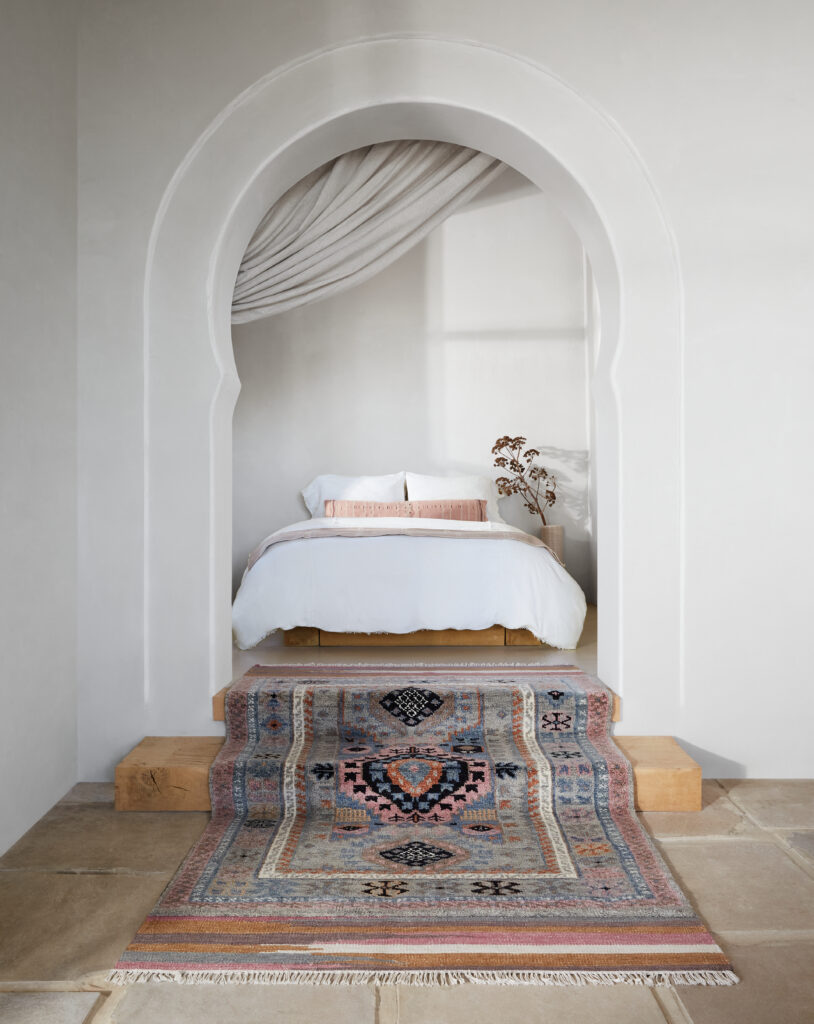 A colorful patterns rug in a bedroom with an architectural archway
